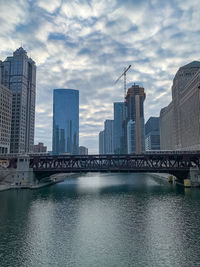 Bridge over river by buildings against sky in city