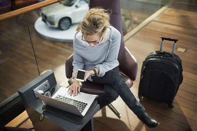 High angle view of businesswoman using laptop and smart phone at airport lobby