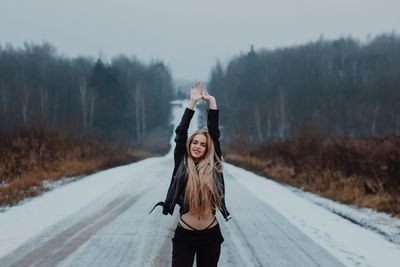 Portrait of young woman with arms raised standing on road during winter
