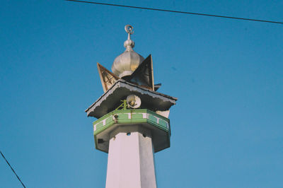 Low angle view of clock tower amidst buildings against clear blue sky