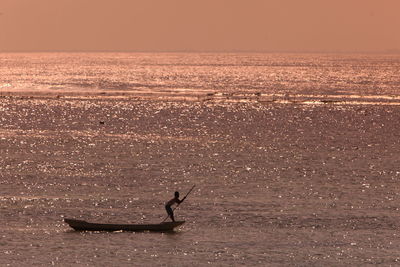 Boy rowing boat in sea against sky during sunny day