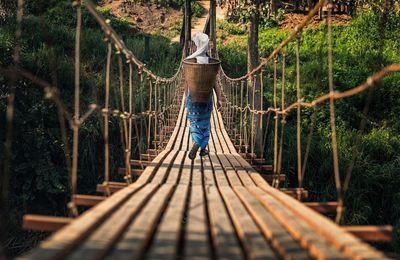 Rear view full length of woman carrying basket on rope bridge