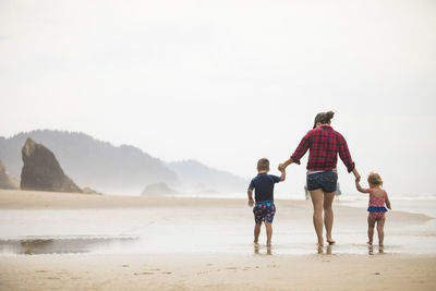 Rear view of mother walking on beach with her two young children.