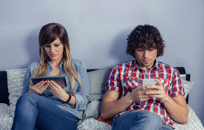 High angle view of couple using digital tablet while leaning on bed at home