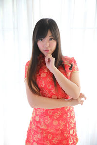 Portrait of beautiful young woman standing against red wall