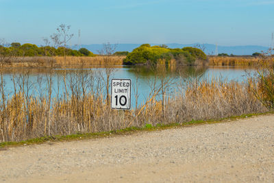 Road sign by lake against sky