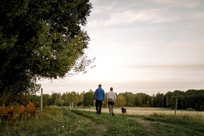 Rear view of couple with dog walking on field at sunset