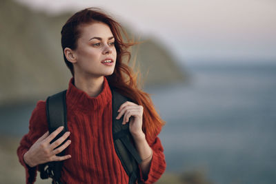 Young woman looking away while standing against sea