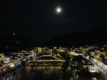 Illuminated bridge over river in city against sky at night