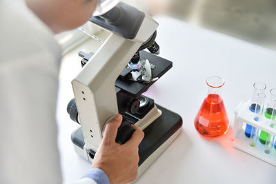 Midsection of person using microscope by test tubes and beaker on table