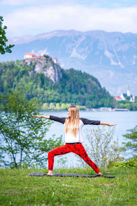 Full length of young woman exercising by lake on field