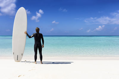 Rear view of woman standing at beach against sky