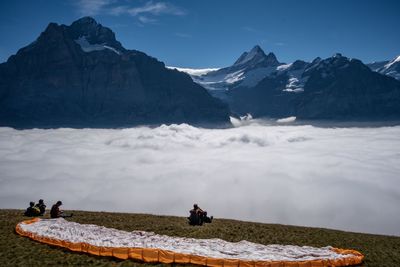 People sitting on field by cloudscape against mountains