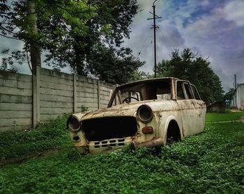 Abandoned car on field against sky