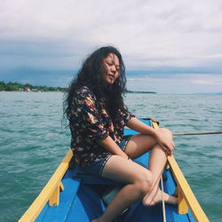 Beautiful young woman sitting on boat in sea against sky