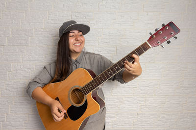 Young woman playing guitar against wall