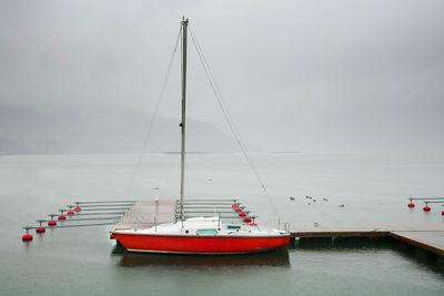 Boat moored by jetty over lake against sky during foggy weather