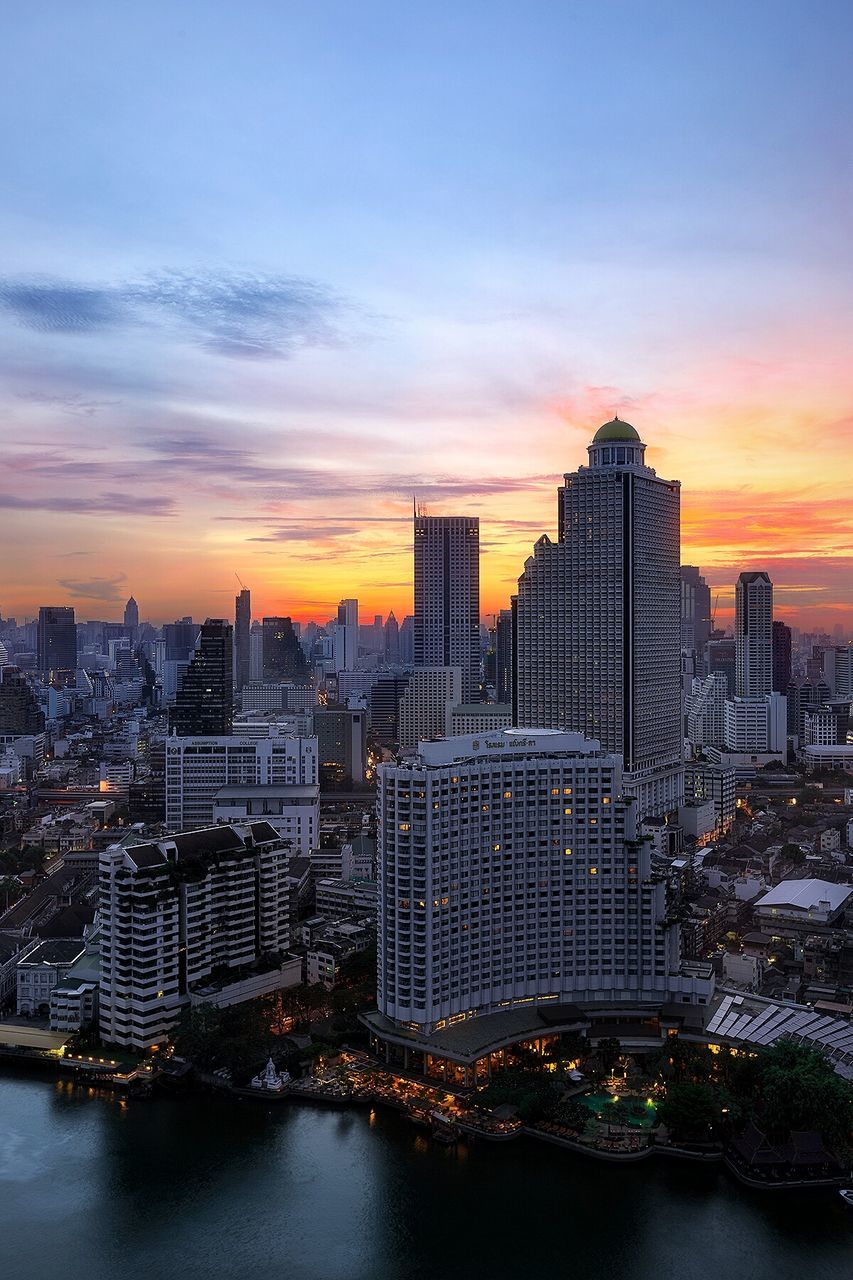 architecture, building exterior, city, built structure, cityscape, sunset, water, skyscraper, orange color, sky, waterfront, tower, illuminated, river, modern, tall - high, residential building, city life, residential district, crowded