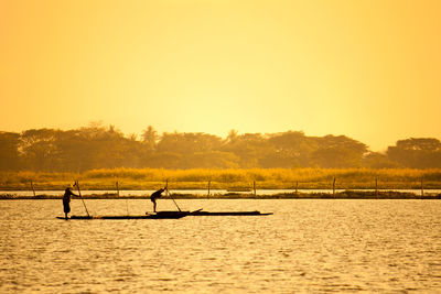 Silhouette people on boat in lake against sky during sunset