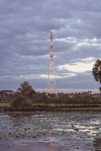 Communications tower by lake against sky