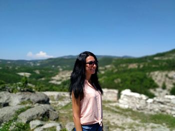 Portrait of young woman wearing sunglasses standing on mountain against sky