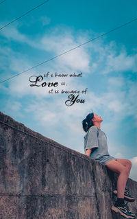 Low angle view of woman sitting on wall against sky