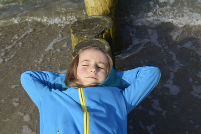 Girl lying on groynes at beach against sky