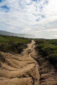 Trail leading out to coastal headlands under blue skies with clouds