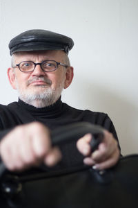 Portrait of senior man wearing flat cap and eyeglasses while holding briefcase at home