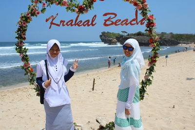 Portrait of friends wearing hijabs standing on shore at beach