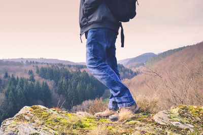 Low section of man standing on mountain against sky during sunset