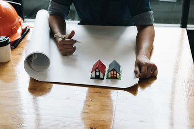 Midsection of architect working on blueprint with model houses on table