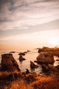 Rocks by sea against sky during sunset