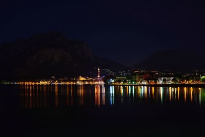 Illuminated town by mountain against sky at night