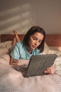 Young woman using digital tablet while lying on bed at home