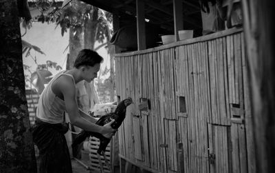 Side view of man with arms raised standing against fence