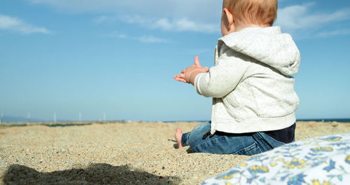 Baby girl standing on sandy beach against sky