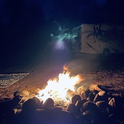 Bonfire by rocks on beach against sky at night