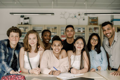 Portrait of smiling professor with teenage students by table in classroom