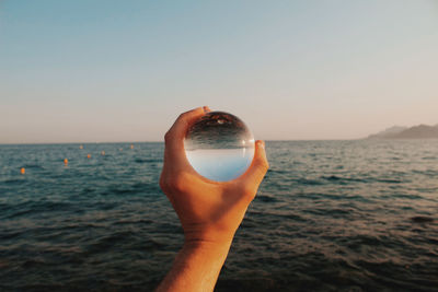 Midsection of person holding sea against sky during sunset