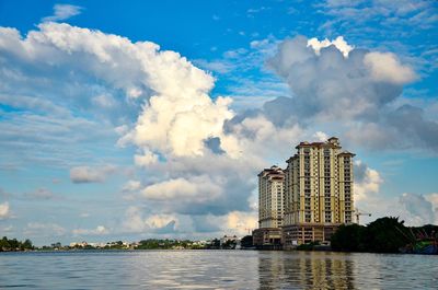 Buildings by river against cloudy sky