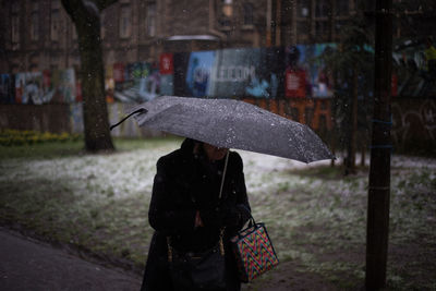 Woman holding umbrella standing on wet street during rainy season