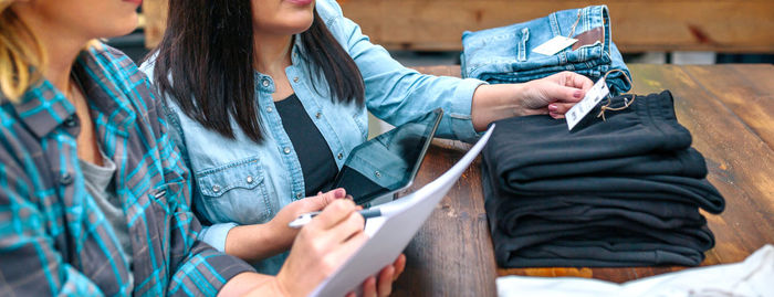 Banner of unrecognizable female entrepreneur checking label of black pants on stack in clothing shop