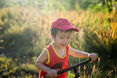 Cute smiling boy riding push scooter against plants