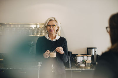 Businesswoman looking at colleague while making tea in office