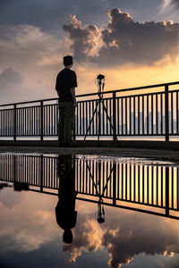 Rear view of man standing on pier against sky during sunset