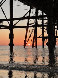 Silhouette bridge over sea against sky during sunset