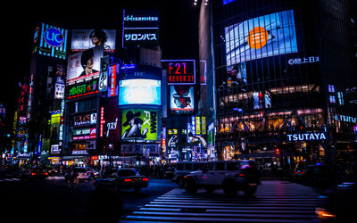 Vehicles on street against illuminated billboards on buildings in shibuya