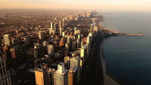 Cityscape by sea against sky during sunset