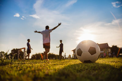 Children playing soccer on field against sky during sunset